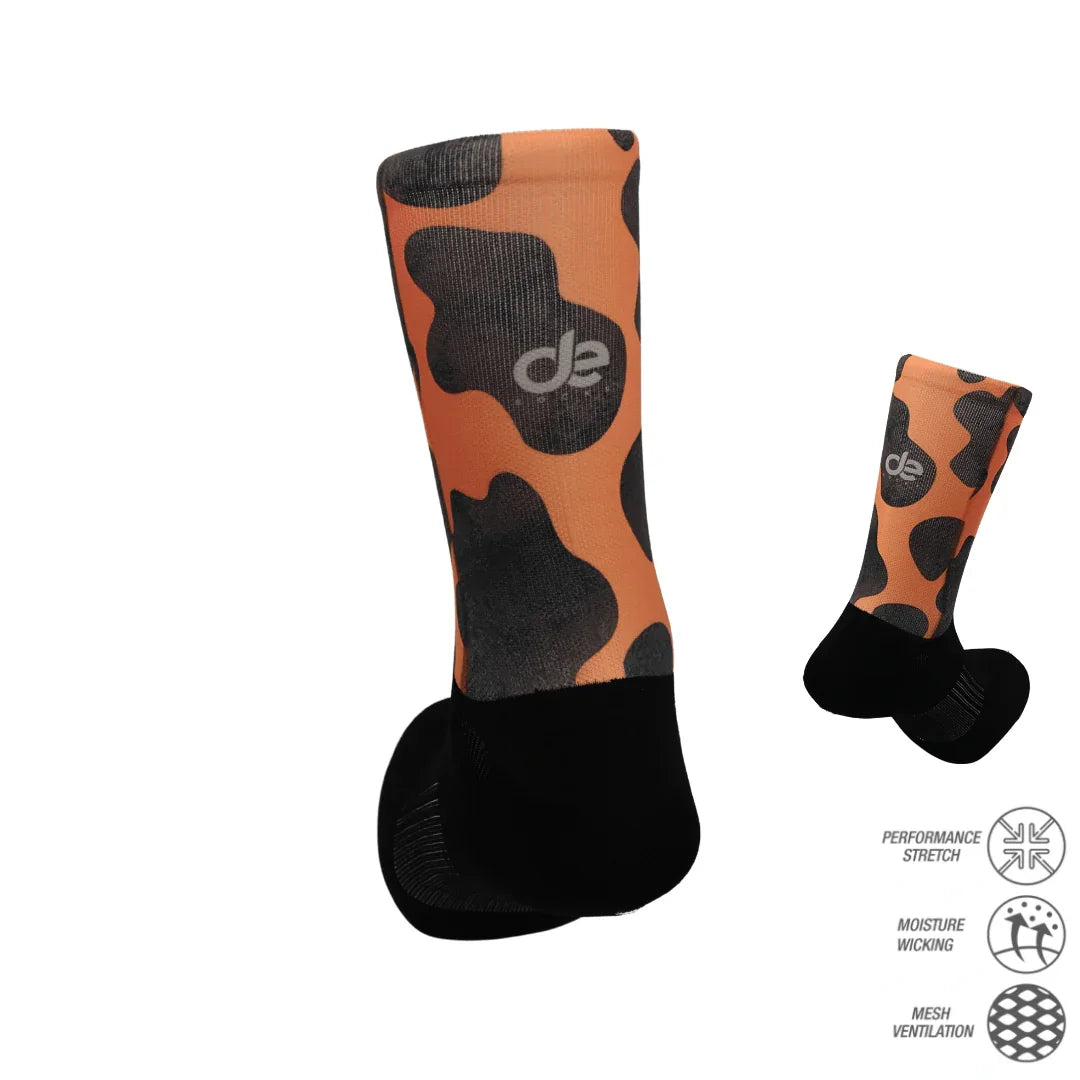 Cow ποδηλατικές κάλτσες-αναπνέουσες με σχέδιο αγελάδας σε πορτοκαλί και μαύρο. Ιδανικές για διαπνοή και άνεση κατά την ποδηλασία.